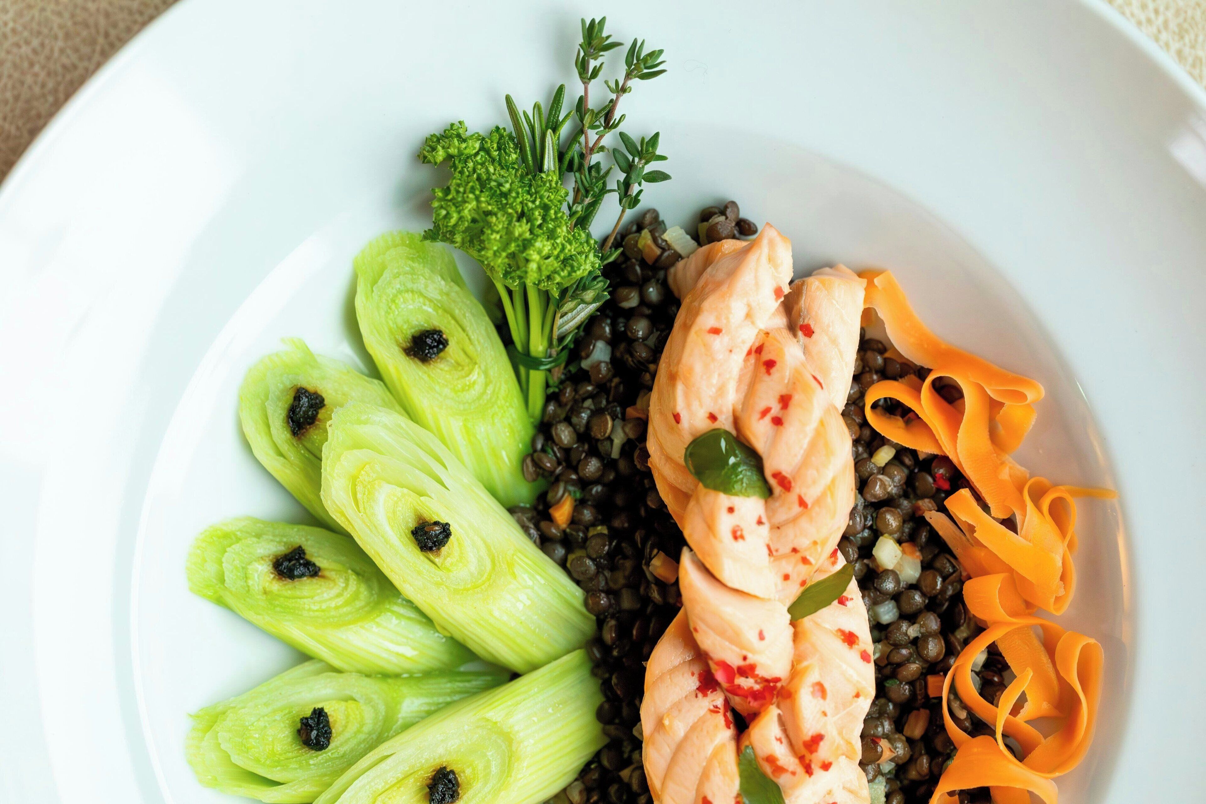 A plate with sliced fennel, salmon, lentils, and carrot ribbons.