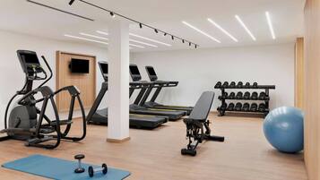 Une salle de sport équipée de tapis de course, de vélos elliptiques, d’un banc de développé couché, d’haltères et d’un grand ballon d’exercice.