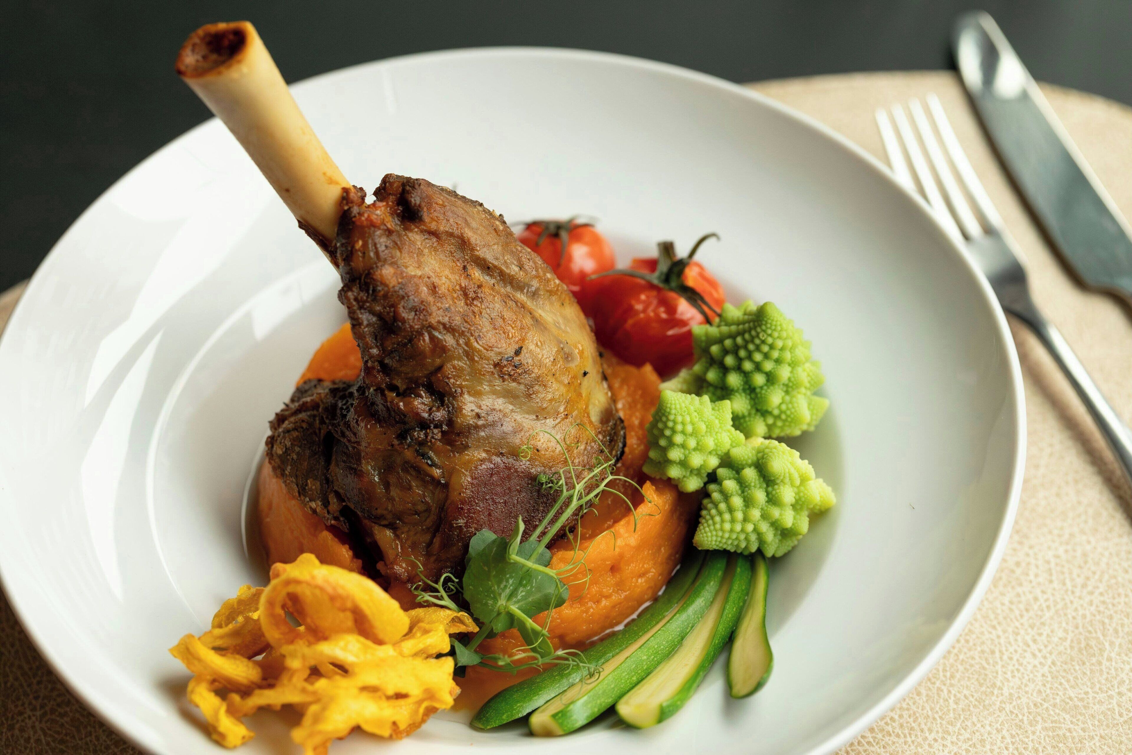 A plate with a roasted leg of lamb, vegetables, and a garnish.