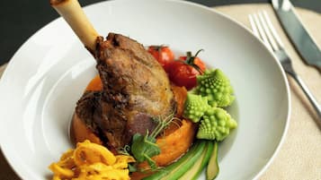 A plate with a roasted leg of lamb, vegetables, and a garnish.