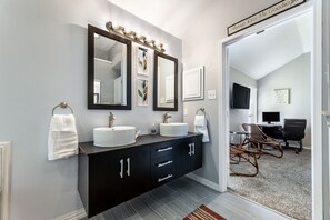 A modern bathroom with two large mirrors, a dark vanity, and a small desk with a chair.