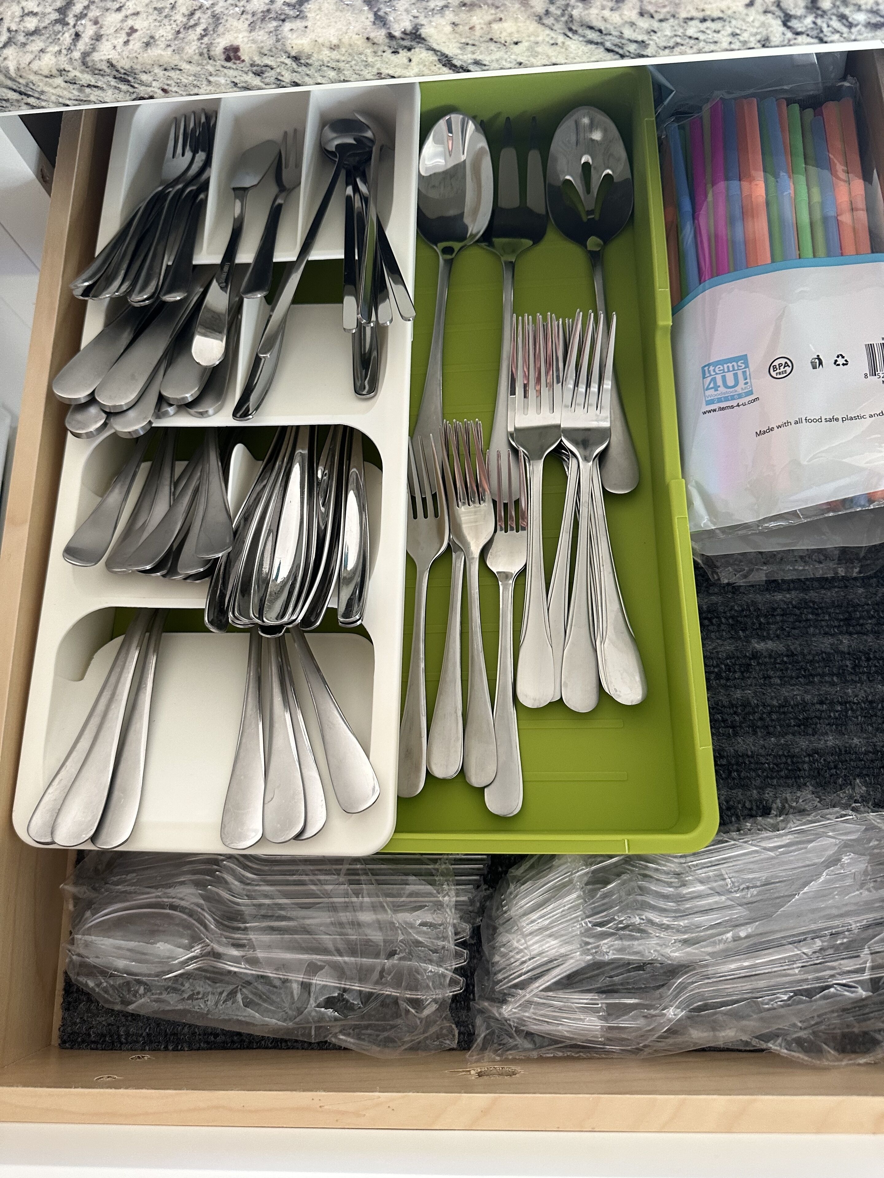 A drawer with neatly organized silverware, including forks, spoons, and knives, and a green tray with plastic utensils.