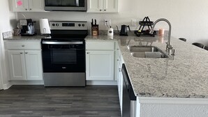Una cocina moderna con armarios blancos, un microondas de acero inoxidable, un horno y una encimera de granito.
