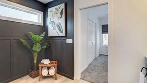 A hallway with dark walls, a large potted plant, a wooden bench with towels, and a framed artwork. - Moorhead Home Rental Near Downtown Fargo! (Moorhead)