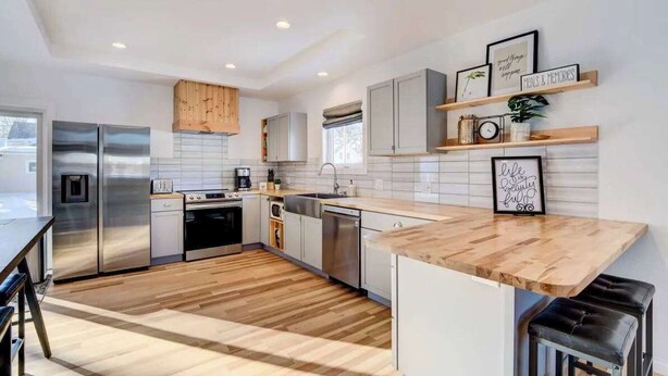 A modern kitchen with stainless steel appliances, wooden flooring, and a bar area. - Moorhead Home Rental Near Downtown Fargo! (Moorhead)
