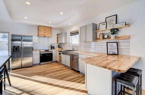 A modern kitchen with stainless steel appliances, wooden flooring, and a bar area. - Moorhead Home Rental Near Downtown Fargo! (Moorhead)