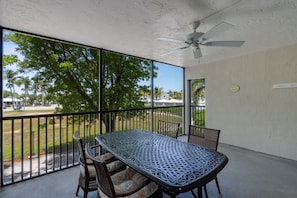 A covered patio with a table and chairs, a ceiling fan, and a view of trees and a parking lot.