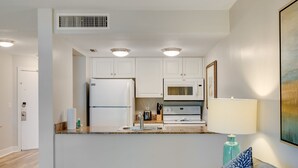 Une cuisine moderne avec des armoires blanches, un réfrigérateur, un four à micro-ondes et une cuisinière. On y trouve un évier avec un robinet, ainsi qu’un plan de travail sur lequel sont posés une lampe et un vase bleu.