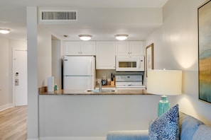 Une cuisine moderne avec des armoires blanches, un réfrigérateur, un four à micro-ondes et une cuisinière. On y trouve un évier avec un robinet, ainsi qu’un plan de travail sur lequel sont posés une lampe et un vase bleu.