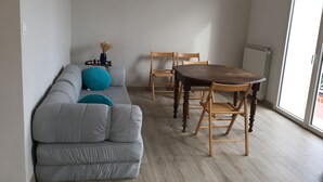 Ein Wohnzimmer mit einem grauen Sofa, zwei blauen Kissen, einem Holzesstisch und vier Holzstühlen.