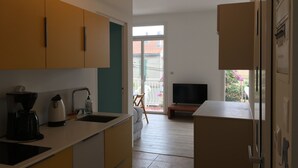Eine moderne Küche mit Spüle, Kaffeemaschine und Schränken. Im Wohnbereich befindet sich ein Fernseher und ein Balkon mit Blick auf die Nachbarschaft.