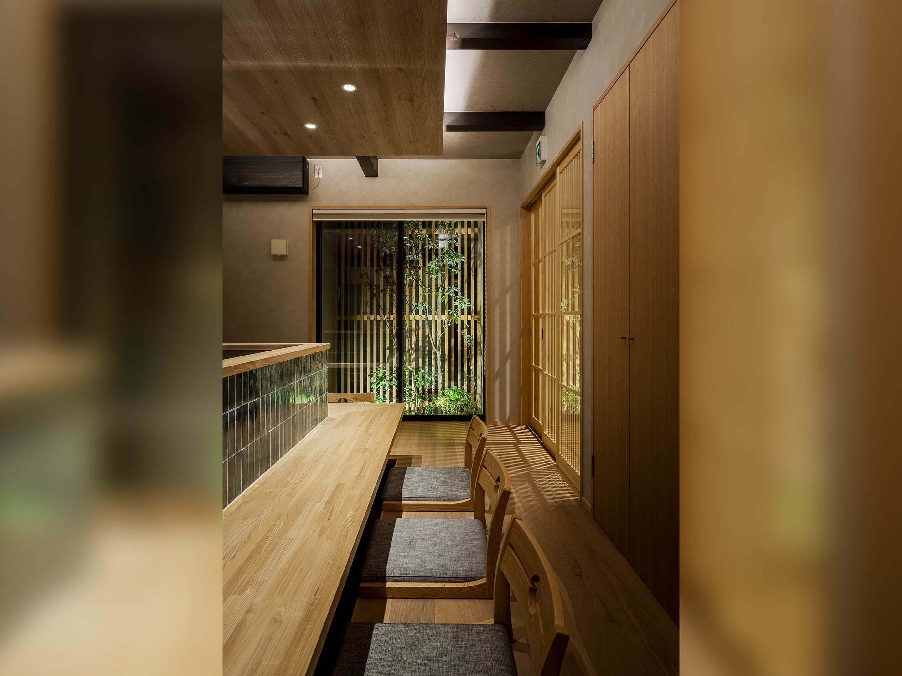Un interior moderno con un mostrador de recepción de madera, una zona de estar con cojines y una puerta corrediza que da a un jardín.