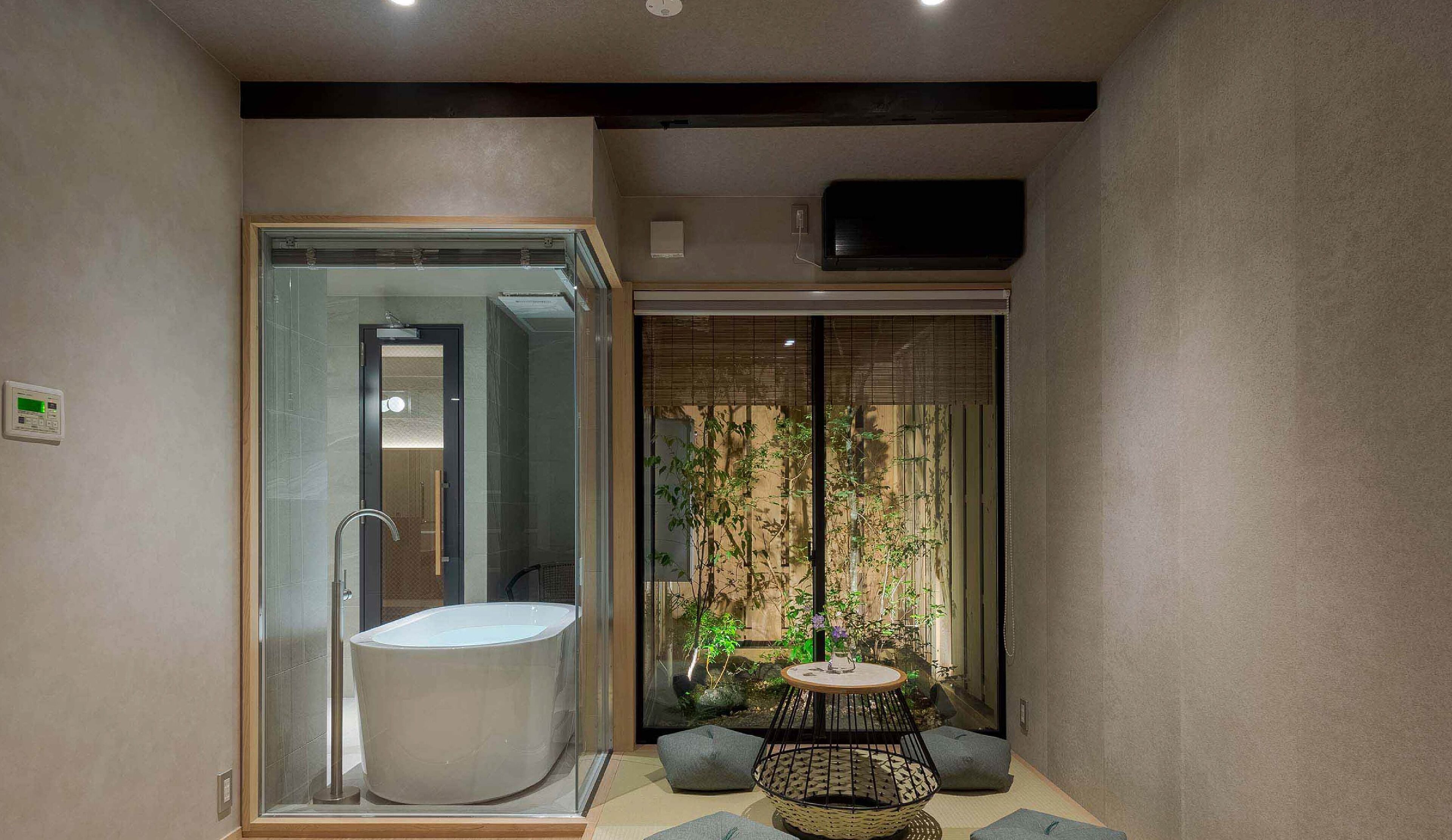 A modern bathroom with a glass-enclosed shower, a bathtub, and a small seating area with a table and plants.