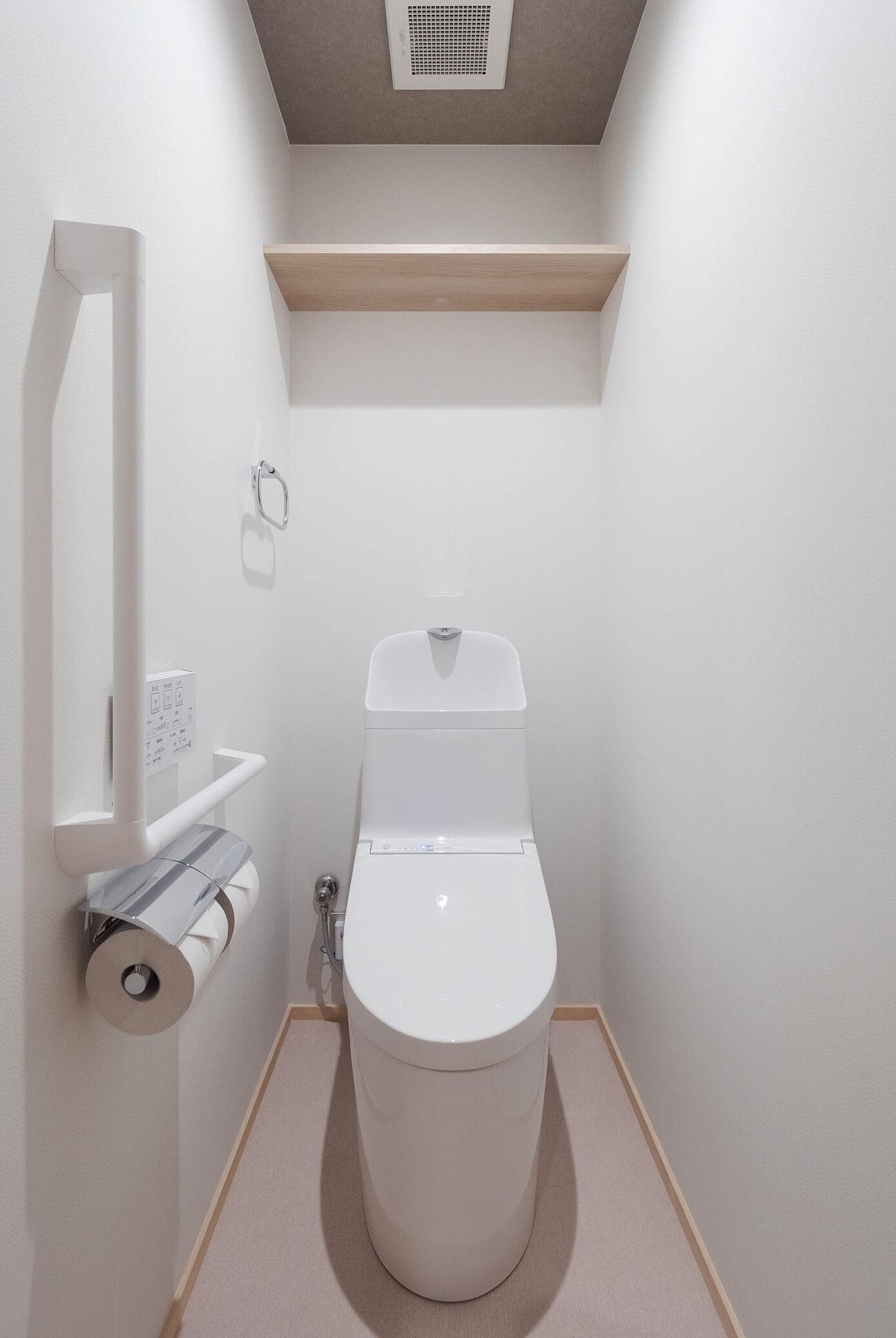 A compact bathroom with a toilet, a toilet paper holder, and a shelf above the toilet.