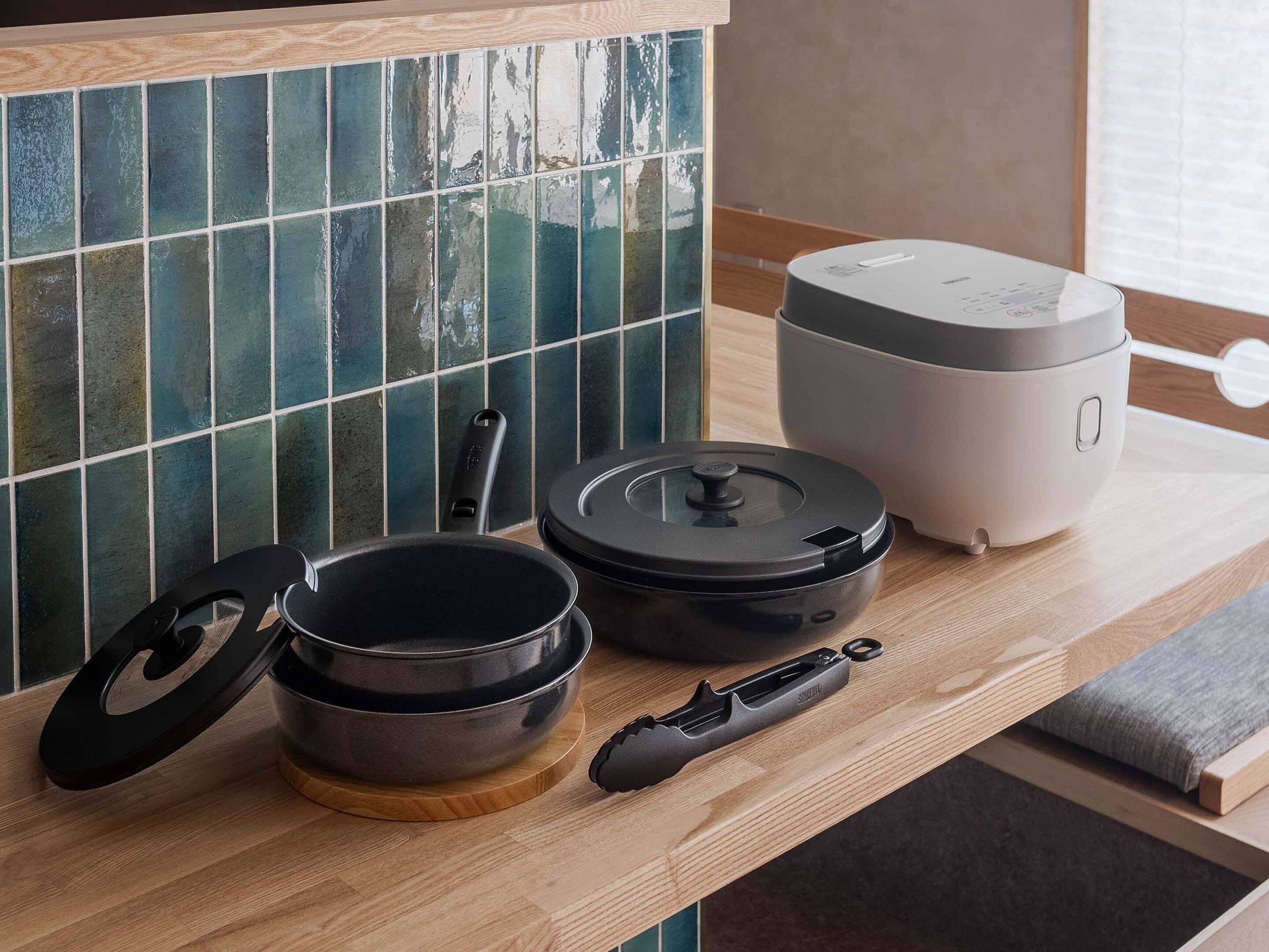 A kitchen counter with a rice cooker, a pan, and a pot.