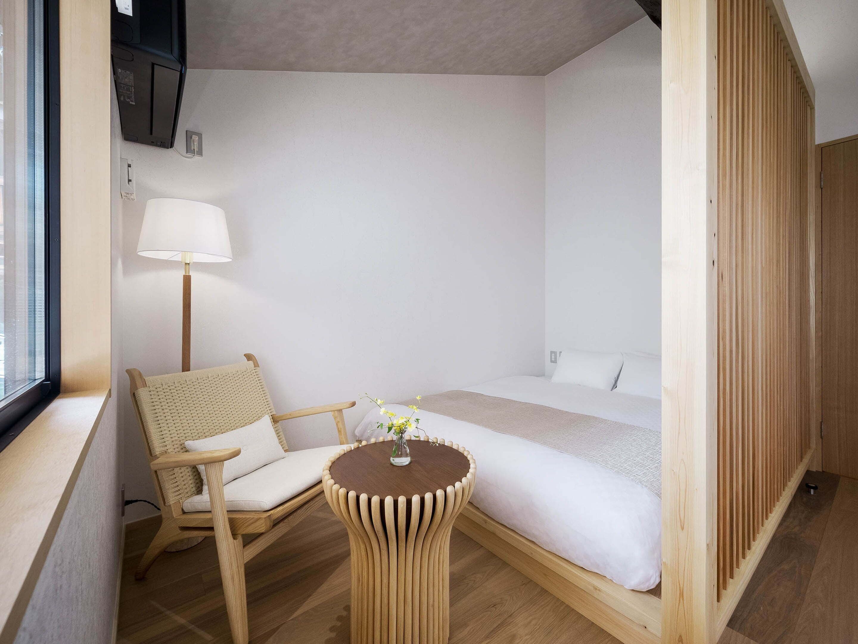 A compact room with a bed, a chair, a small table, and a lamp.