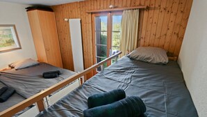 A room with two beds, wooden walls, a window with curtains, and a framed picture on the wall. - Joli Appartement Proche du Centre (Nendaz)