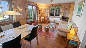 A cozy room with a wooden dining table set for four, a sofa, a TV, and a lamp. - Joli Appartement Proche du Centre (Nendaz)