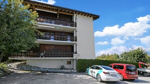 A multi-story building with balconies, a parking area with cars, and a clear sky. - Joli Appartement Proche du Centre (Nendaz)