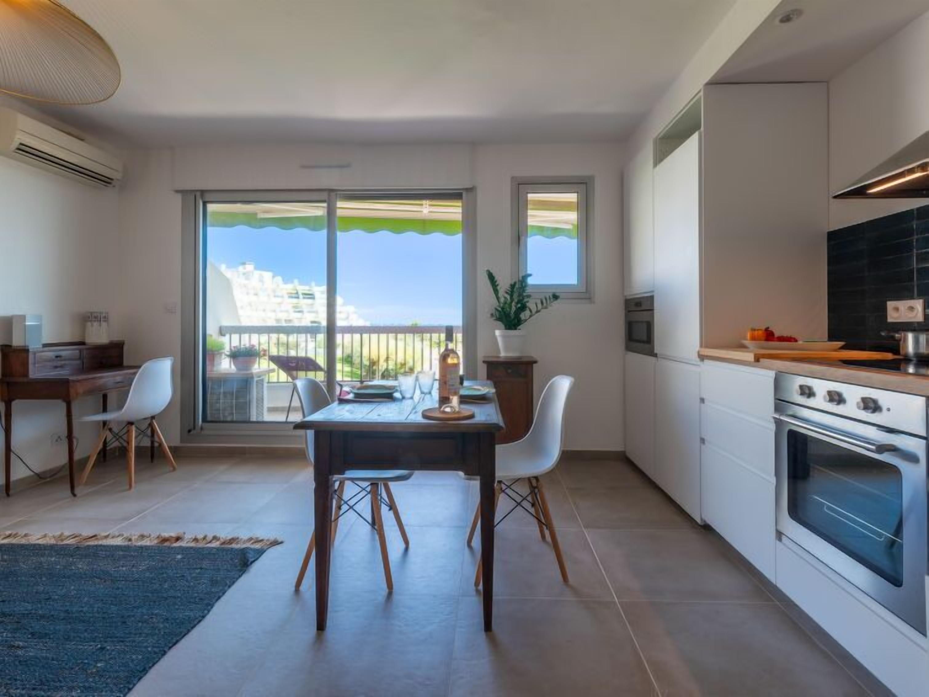 A modern kitchen with a large oven, a dining area with a table and chairs, and a balcony with a view of buildings.