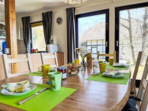 A dining area with a wooden table set for two, featuring a green placemat, a glass of juice, a cup, a plate with food, and a vase with flowers. - Grandma by Interhome (Frankenau)