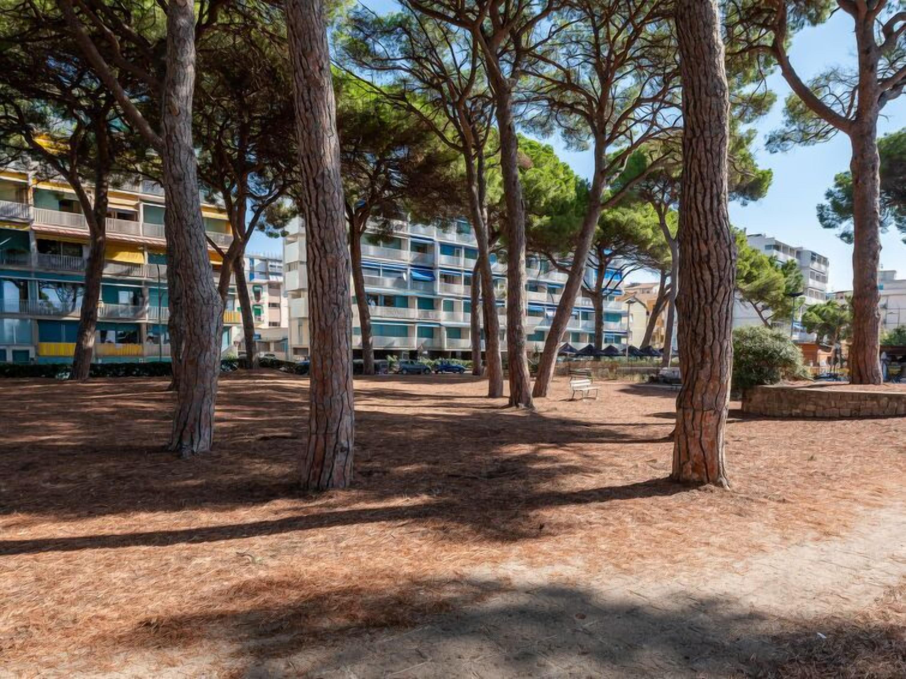 A park with tall trees and a row of multi-story buildings in the background.