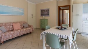 Un salon comprenant un canapé, une table à manger avec des chaises, un buffet et un coin cuisine avec des placards et un réfrigérateur.