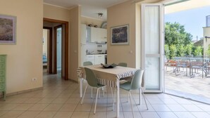 Un coin repas avec une table et des chaises, une cuisine à l’arrière-plan et une vue sur l’extérieur.