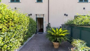 Un étroit sentier pavé mène à l’entrée d’un bâtiment, où se trouve une porte.
