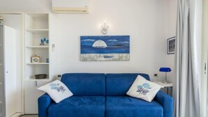 Ein Wohnzimmer mit einem blauen Sofa, einem Bild eines Bootes auf dem Wasser und einer weißen Klimaanlage an der Wand.