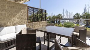 Eine Terrasse im Freien mit Korbmöbeln, einem weißen Sofa und Blick auf einen Yachthafen mit Booten.