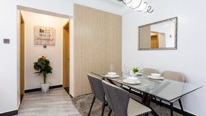 Un espace repas moderne avec une table en verre, des chaises grises et un séparateur en bois.