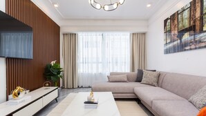 Un salon moderne avec un canapé d’angle, un téléviseur à écran plat, une table basse en marbre et une grande fenêtre agrémentée de rideaux.