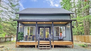 A two-story cabin with a porch, large windows, and a wooden deck.