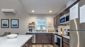 A modern kitchen with a central island, stainless steel appliances, and a window with blinds.