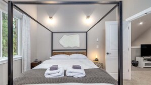 A modern bedroom with a four-poster bed, a white fur rug, and a mounted artwork on the wall.