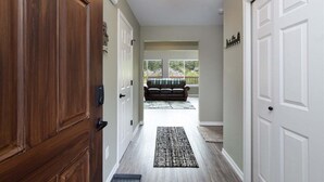 A hallway with wooden doors, a black and white rug, and a view to a balcony with a couch. - Timbers Edge | Quaint Oasis ~ Hot Tub ~ EV Charger (Packwood)