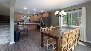 A modern kitchen with wooden cabinets, a stainless steel refrigerator, and a dining area with a wooden table and chairs. - Timbers Edge | Quaint Oasis ~ Hot Tub ~ EV Charger (Packwood)