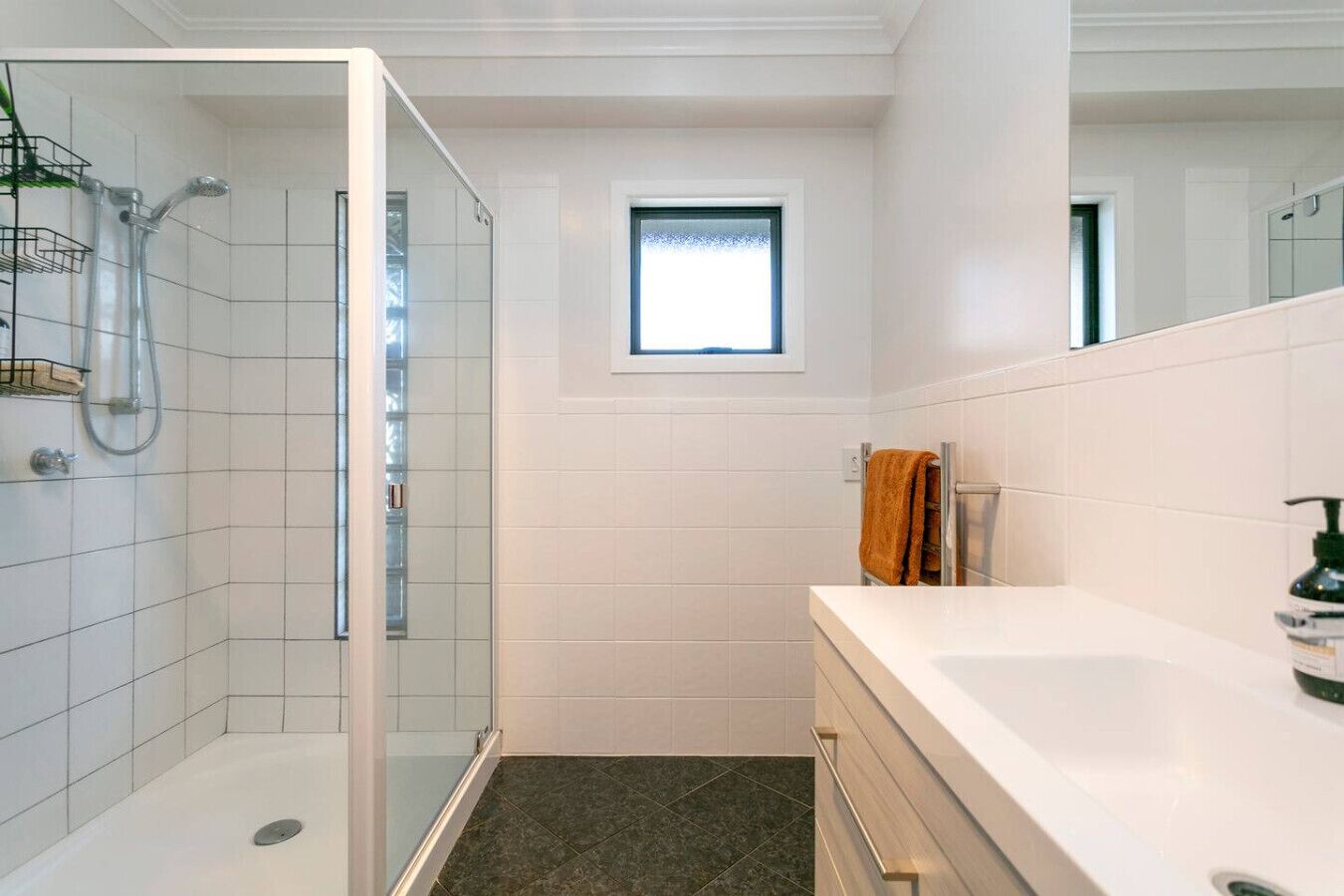 Ein modernes Badezimmer mit einer Duschkabine aus Glas, einem kleinen Fenster und einem weißen Waschtisch mit Spiegel.