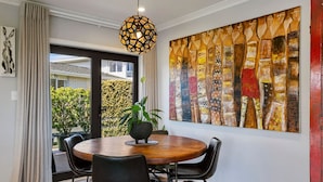 Uma sala de jantar com uma mesa redonda de madeira, cadeiras pretas, um vaso com planta e um quadro abstrato grande na parede.