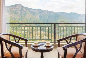 Ein Balkon mit zwei Stühlen und einem kleinen Tisch, mit Blick auf eine gebirgige Landschaft.