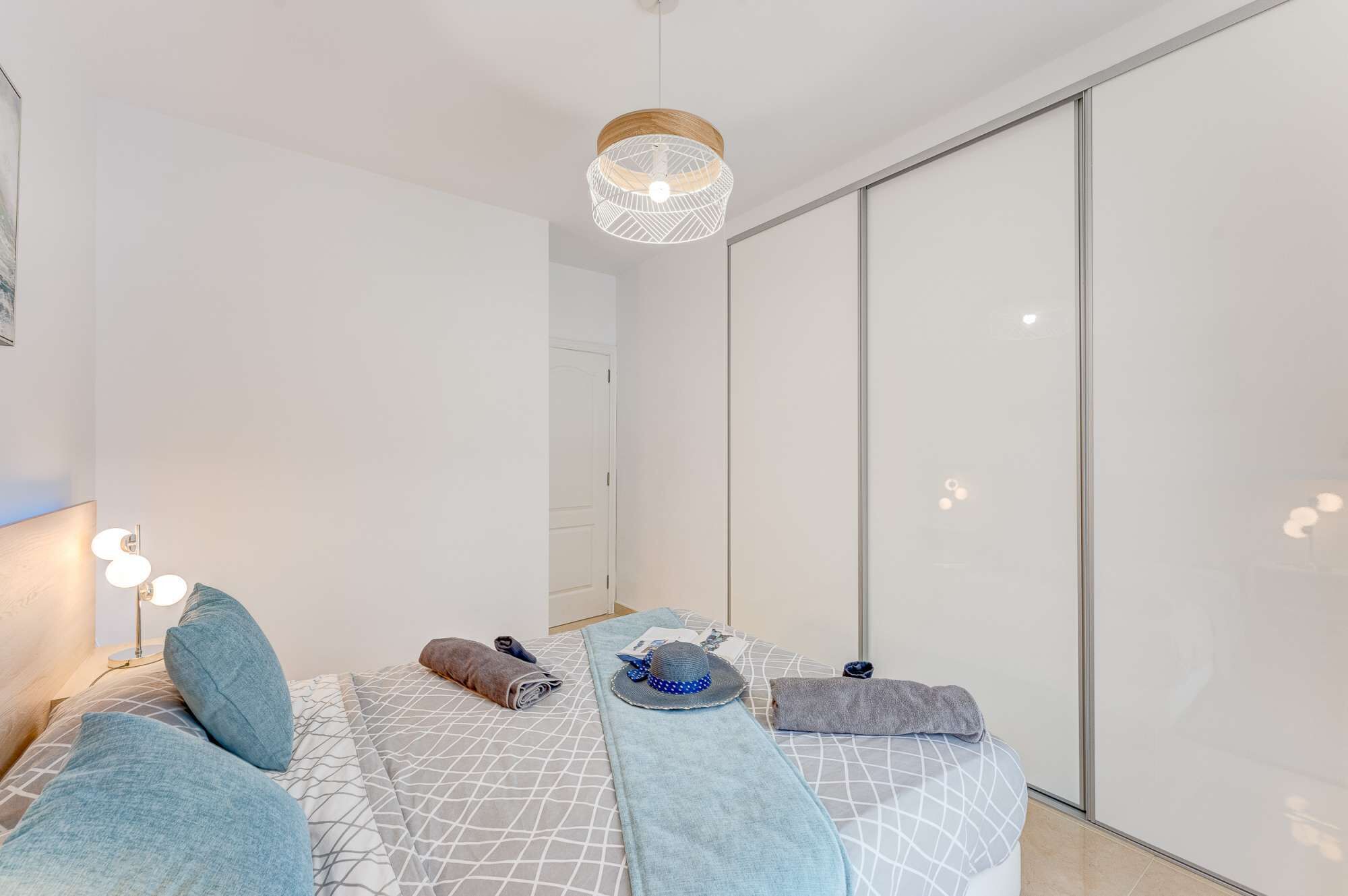 Une chambre à coucher moderne avec un lit, un luminaire suspendu, une armoire et une table de chevet avec une lampe.