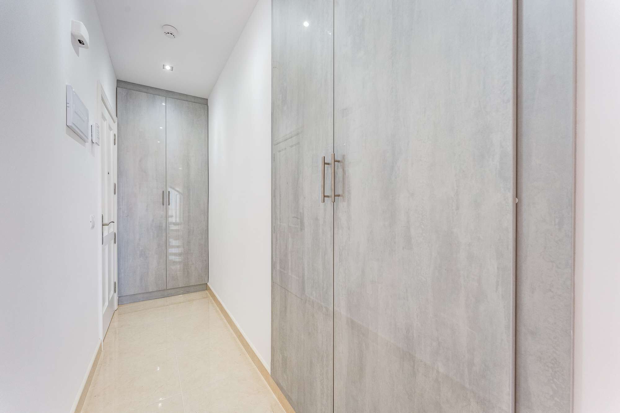 A hallway with a light-colored tiled floor and a large wardrobe with a metallic handle.