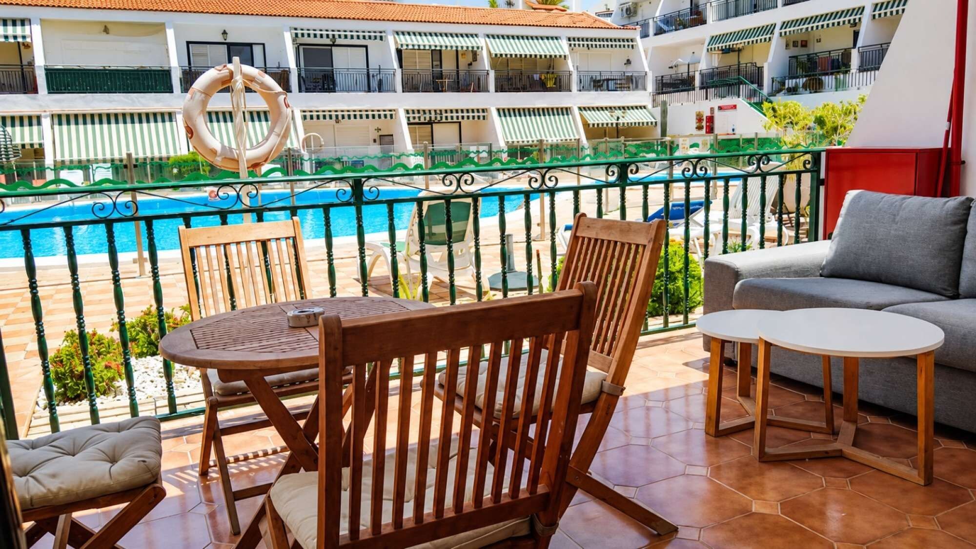 A balcony with a pool view, wooden furniture, and a sofa.