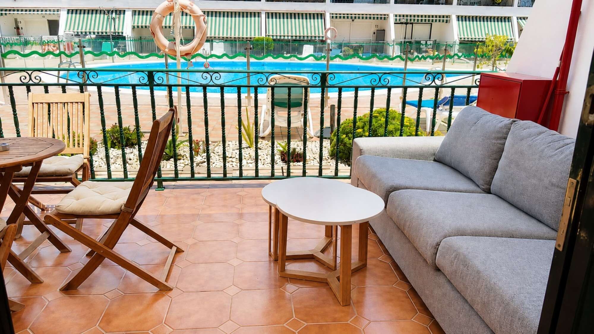 A balcony with a pool, a sofa, a table, and chairs.