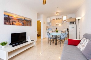 Un salon moderne doté d’un téléviseur à écran plat, d’un canapé agrémenté de coussins à motifs et d’un coin repas avec une table et des chaises.