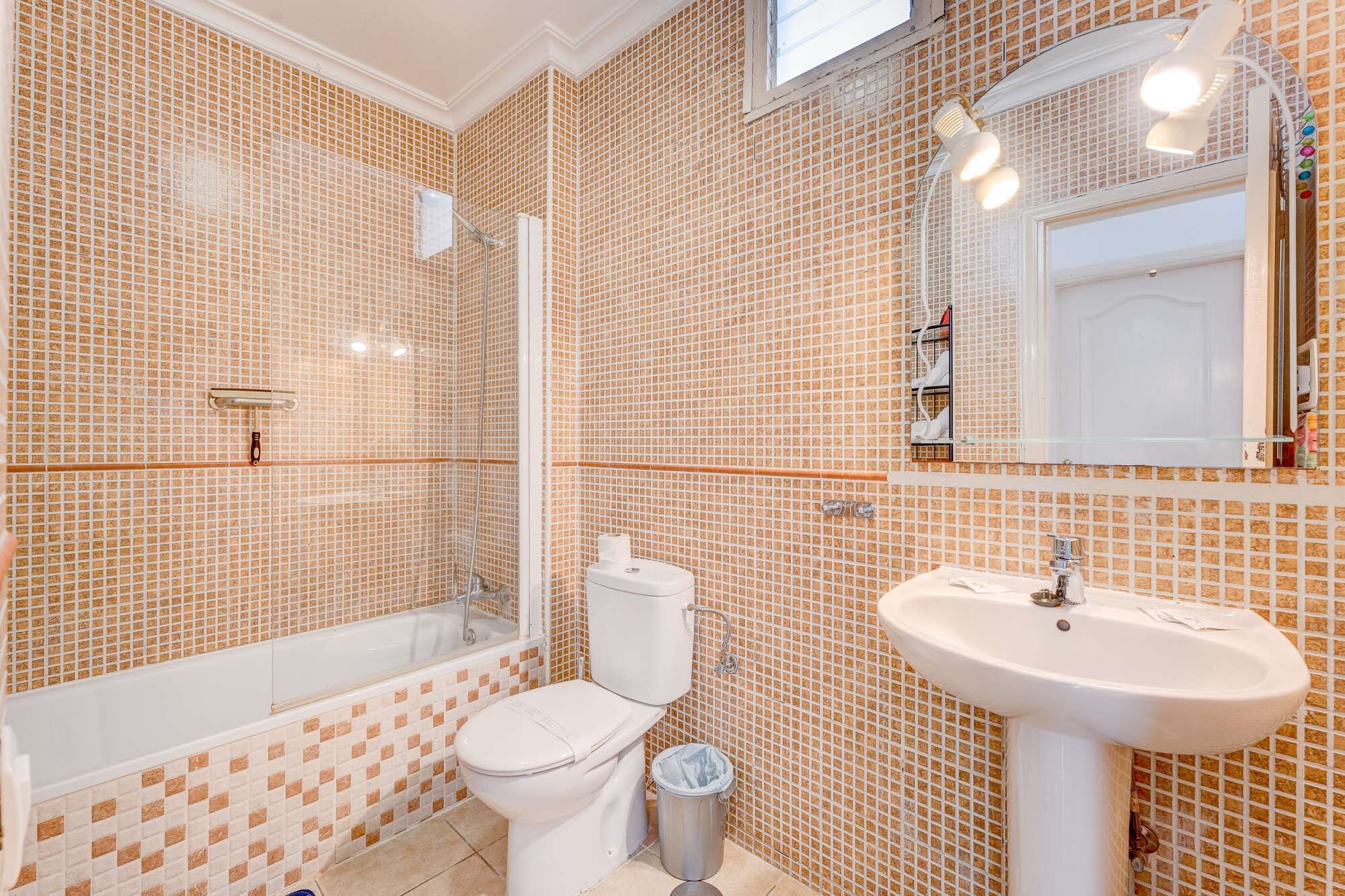 A bathroom with a bathtub, toilet, and sink, all with matching mosaic tile walls.