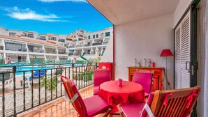 Ein Balkon mit rotem Tisch und Stühlen, mit Blick auf einen Pool und Gebäude.