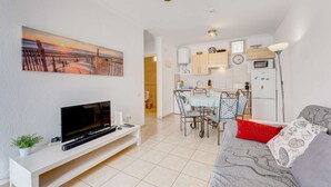 Ein kompakter Wohnbereich mit Fernseher, Sitzgelegenheit, Küchenzeile und einem Gemälde, das eine Sonnenuntergangsszene zeigt.
