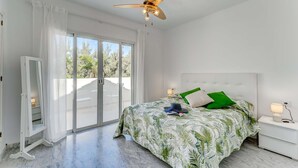 A bedroom with a bed, a nightstand, a ceiling fan, and a sliding glass door leading to a balcony.